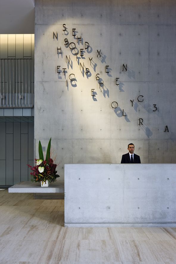 a man sitting behind a reception desk in front of a wall with writing on it