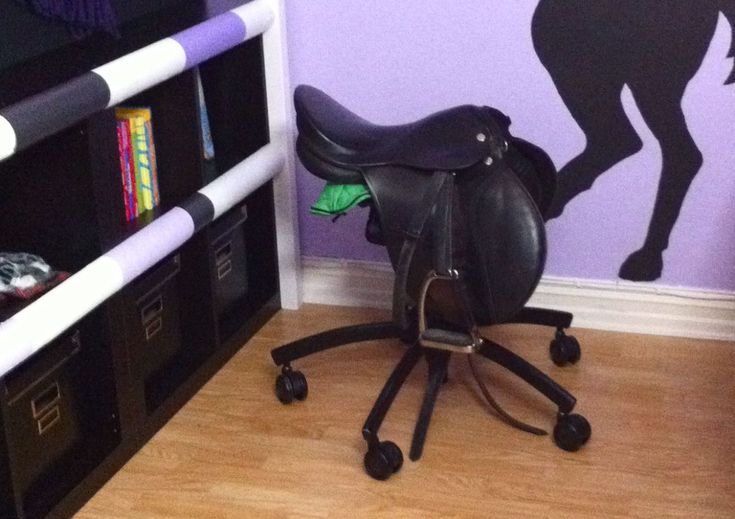 a black horse saddle sitting on top of a wooden chair in front of a purple wall