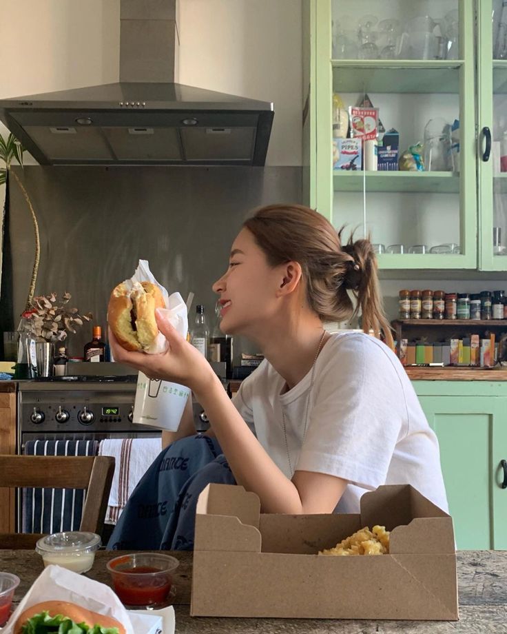 a woman sitting on the kitchen counter eating a sandwich