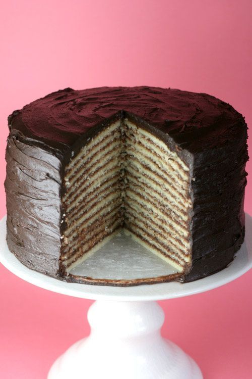 a chocolate cake on a white pedestal with one slice cut out to show the layers