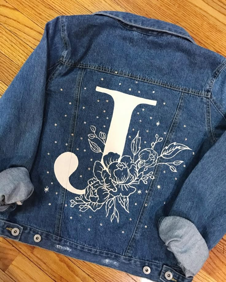 a denim jacket with the letter j painted on it and flowers in the front pocket