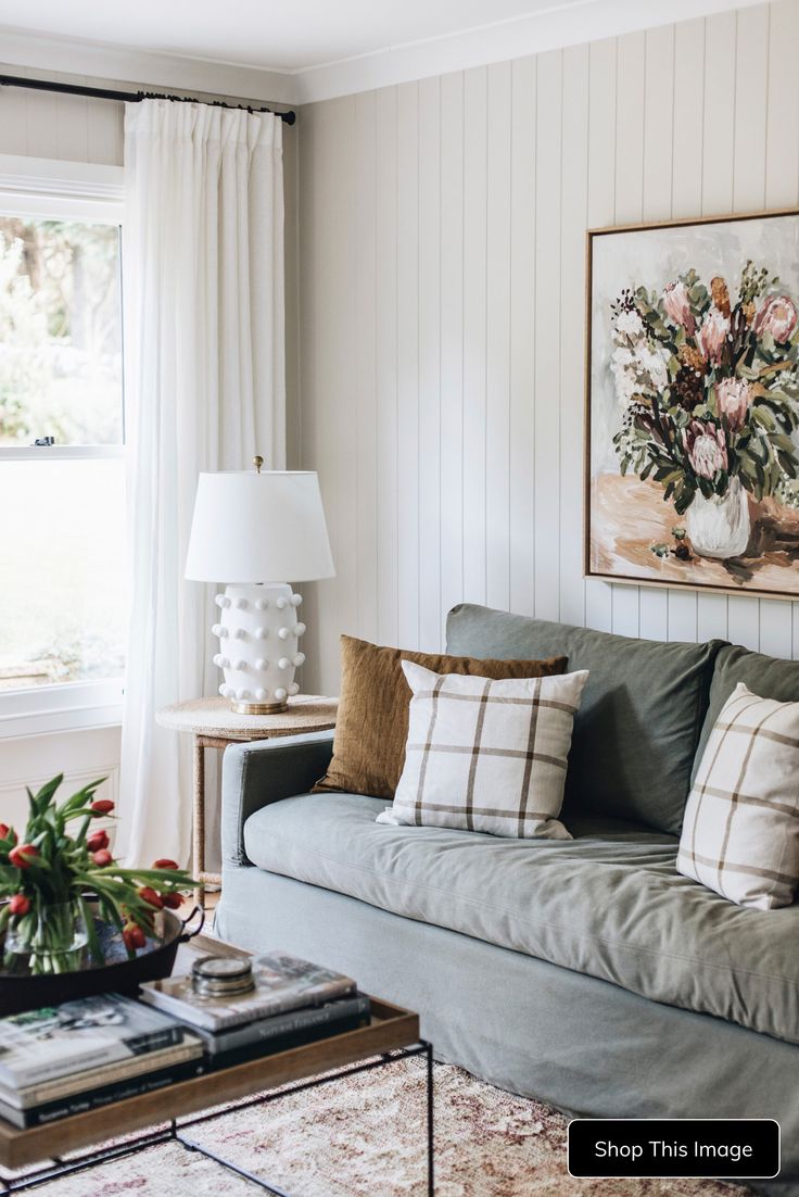 a living room filled with furniture and a painting hanging on the wall above it's windows