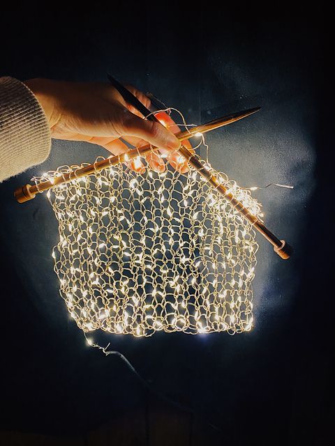 a hand holding a string light bag with two knitting needles in it and some yarn on the handle