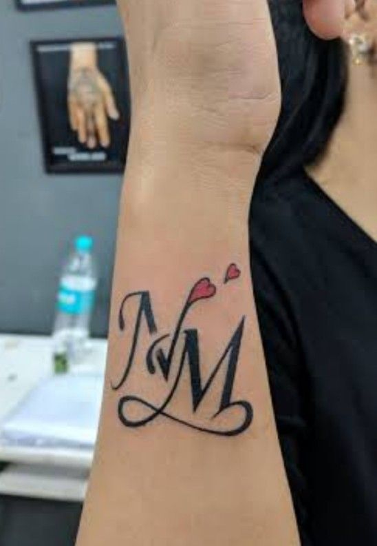 a woman's wrist tattoo with the letter m and hearts on it in black ink