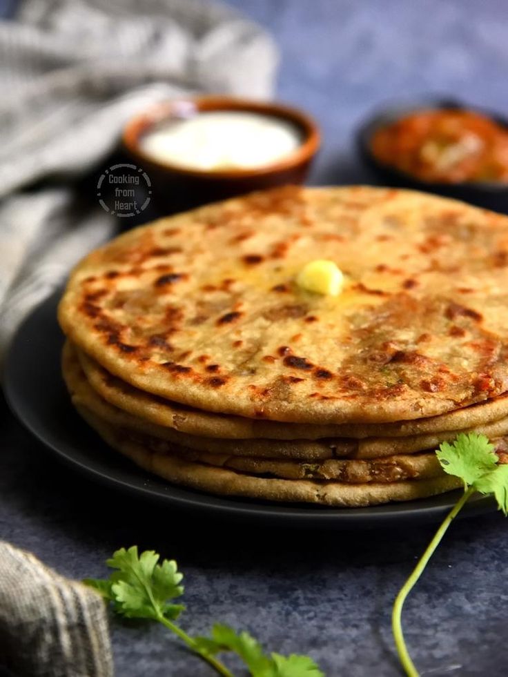 three flatbreads on a black plate with cilantro and yogurt in the background