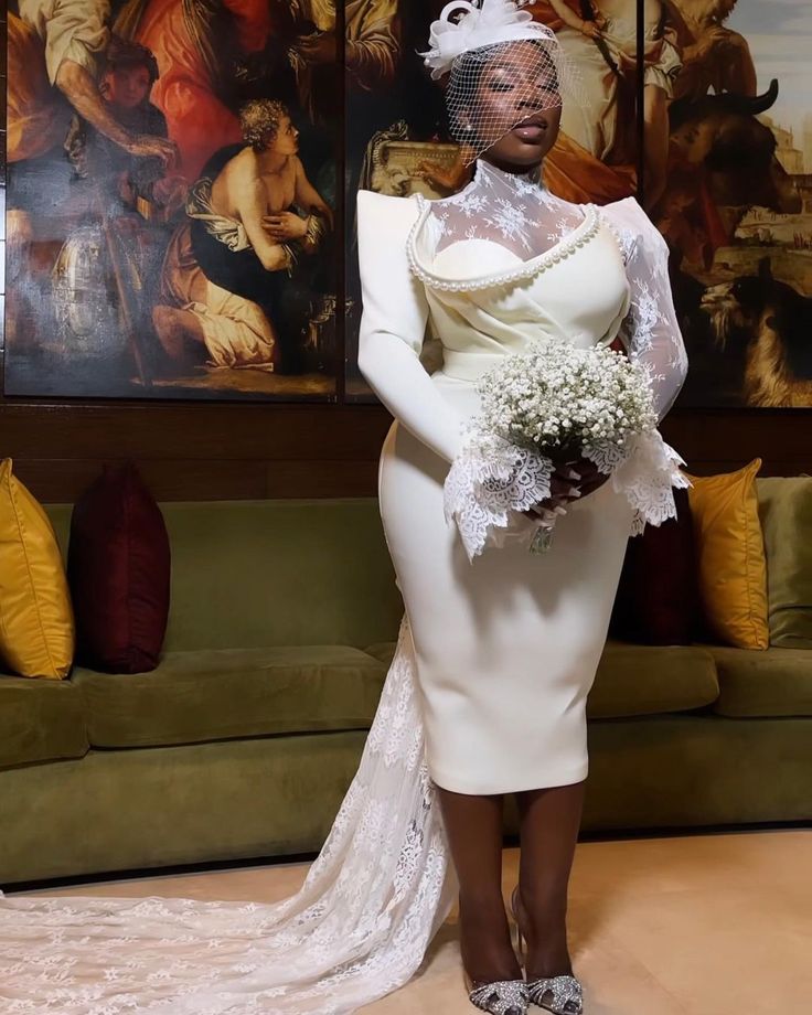 a woman standing in front of a couch wearing a white dress and veil with flowers on her head