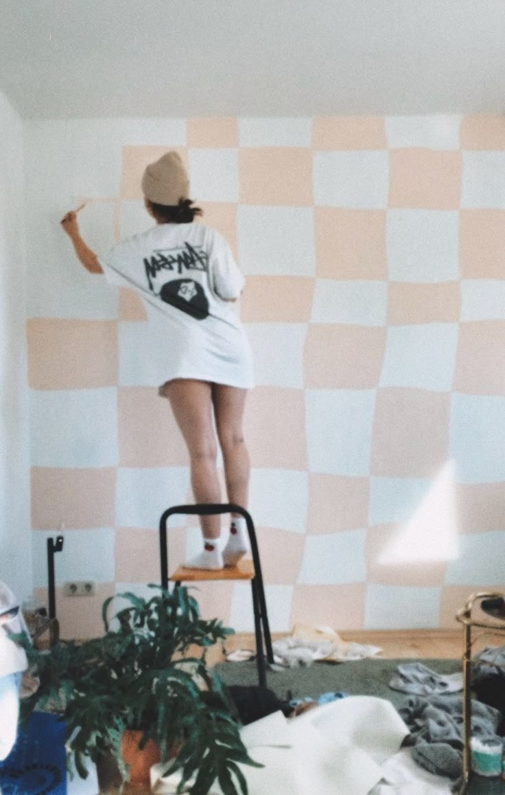 a woman is standing on a ladder in front of a checkered wall and painting the walls