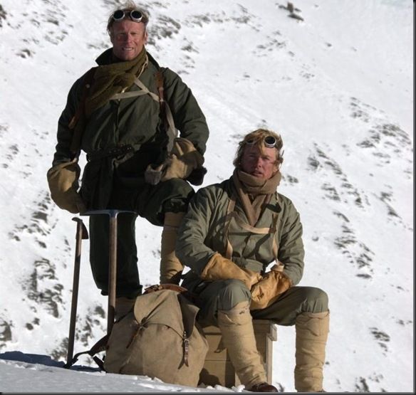 two men sitting on top of a snow covered slope