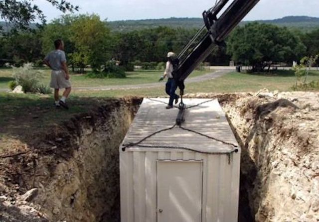 a man standing on top of a wooden box next to a large metal object in the middle of a dirt field