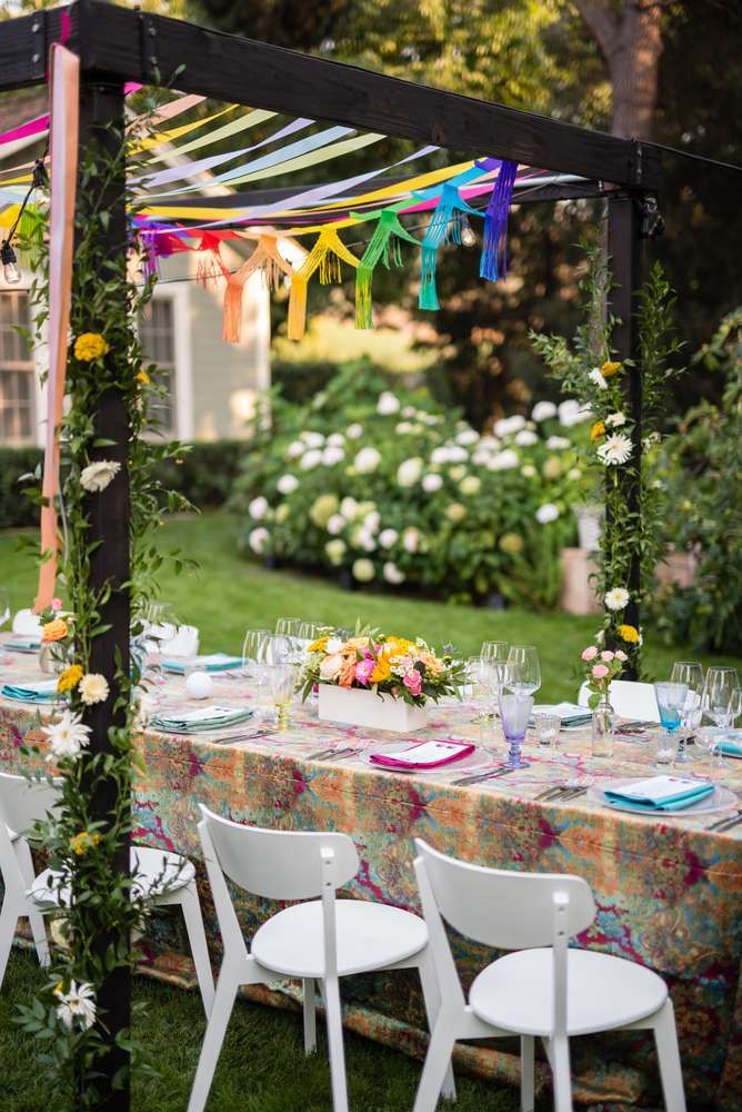 an outdoor table set up for a party with colorful streamers hanging from the ceiling