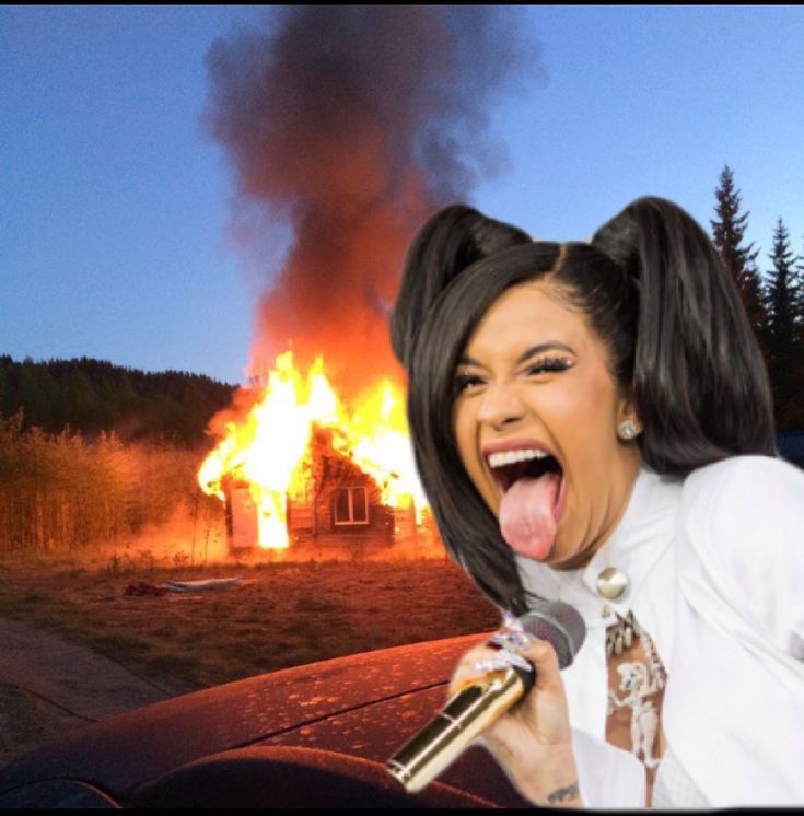 a woman sticking her tongue out in front of a house on fire with a microphone