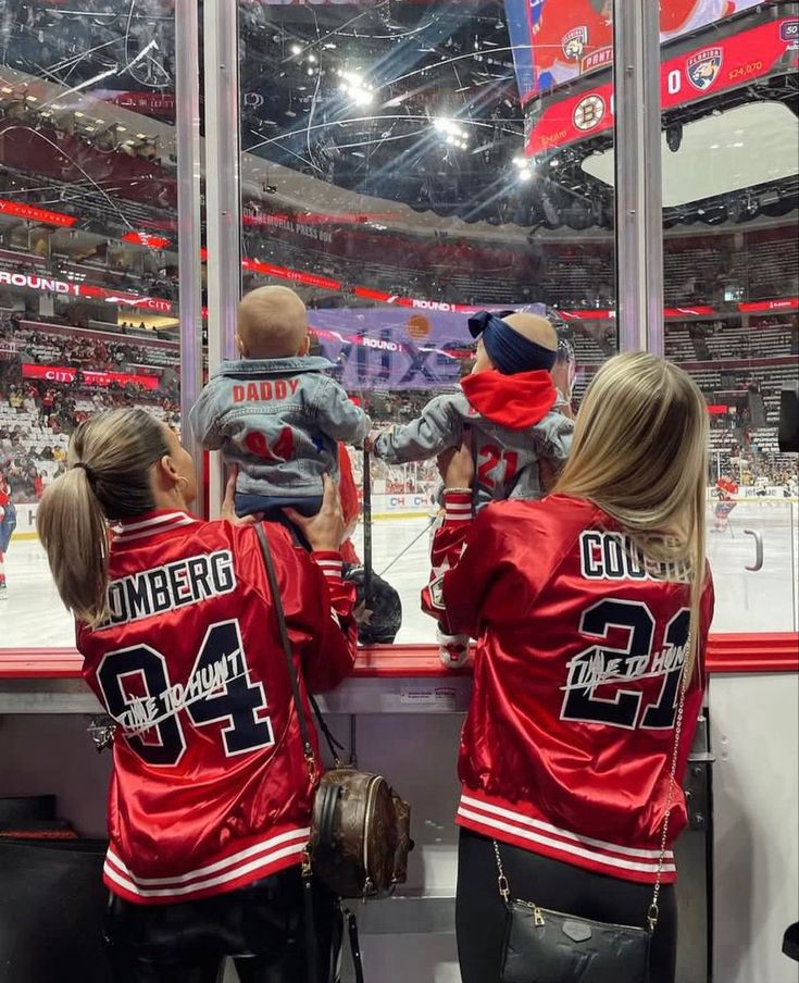 two women and a baby are sitting in front of a window at a hockey game