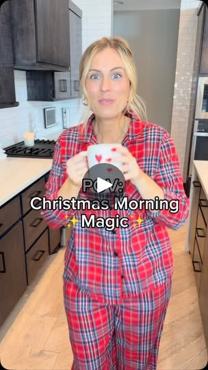 a woman in pajamas is holding a cup and looking at the camera while standing in her kitchen