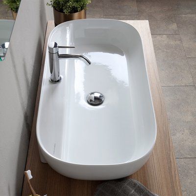 a white sink sitting on top of a wooden counter next to a mirror and potted plant