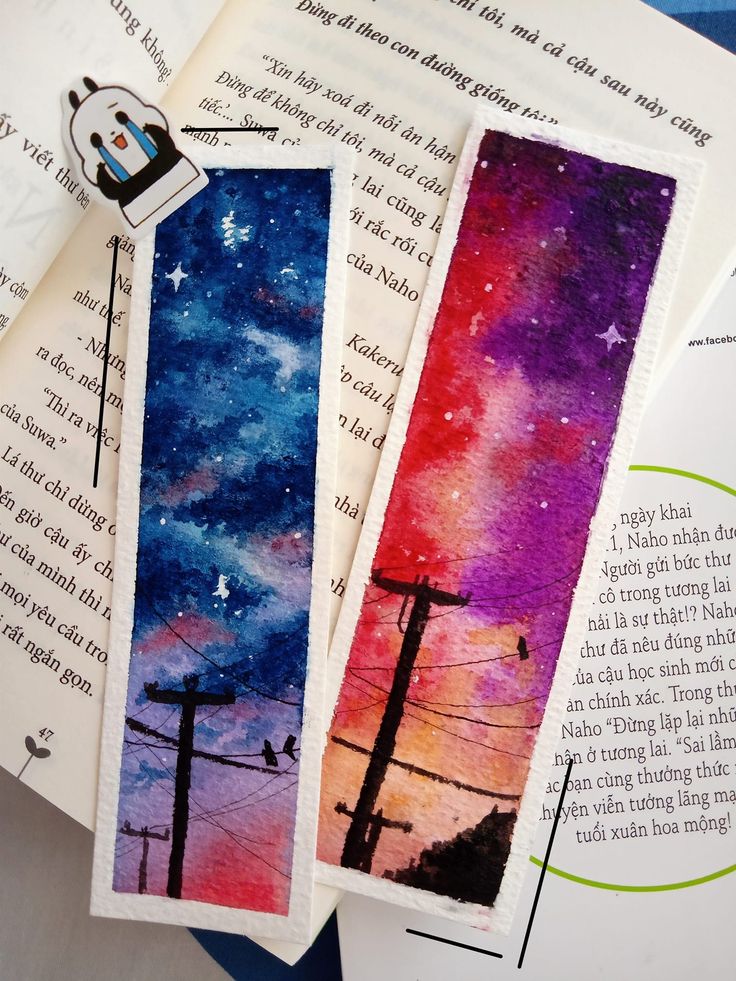 two bookmarks sitting on top of an open book with watercolors and ink