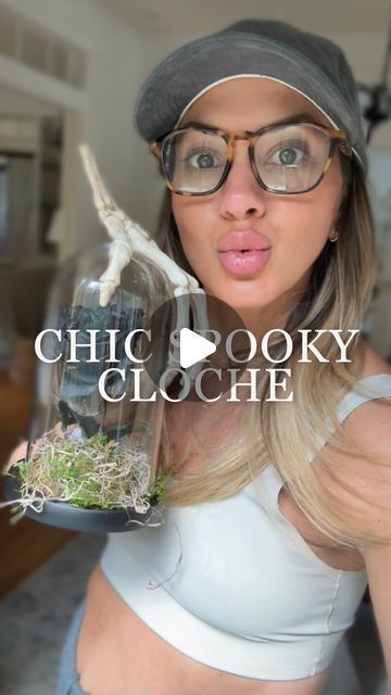 a woman with glasses holding up a fake bird in a glass jar that says chic spooky cloche