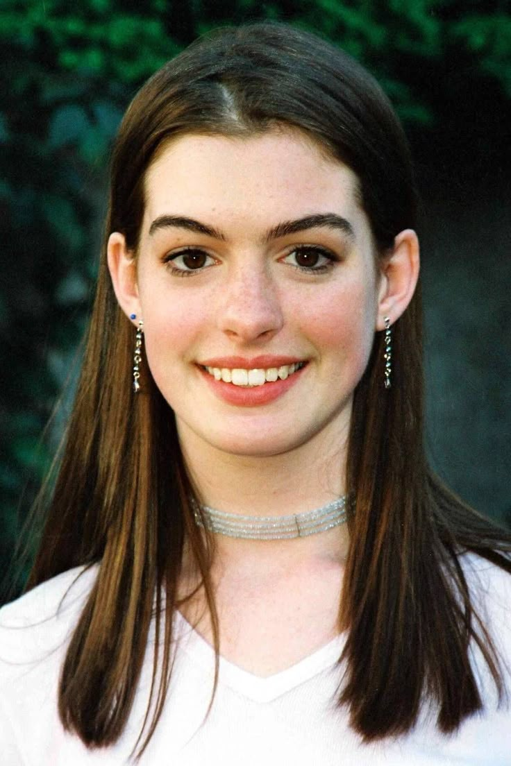 a woman with long hair wearing a white t - shirt and silver jewelry smiling at the camera