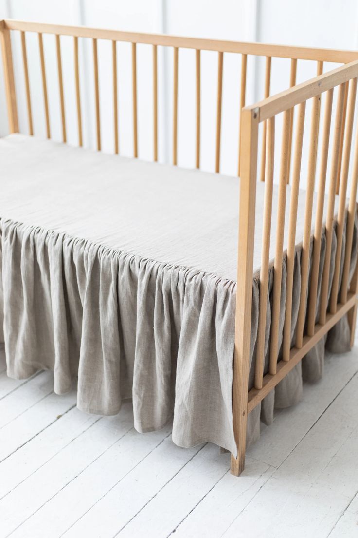 a wooden crib with a gray bed skirt