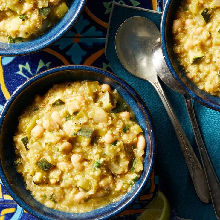 three bowls filled with food sitting on top of a blue and yellow table cloth next to two spoons