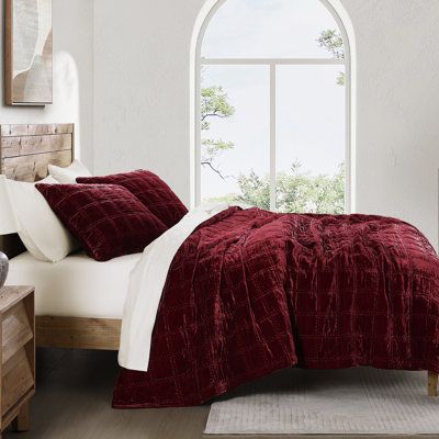 a bedroom with a large window and red bedding in front of a white wall