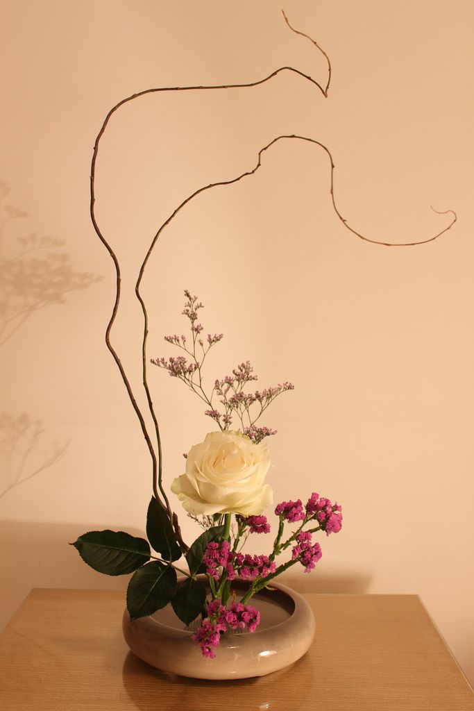 a vase filled with flowers sitting on top of a wooden table next to a wall