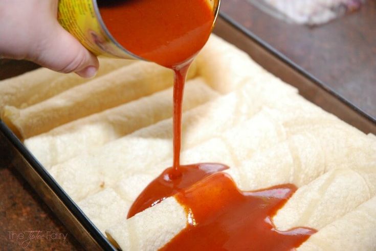 someone pouring sauce on top of bread in a pan