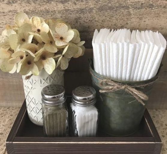 an arrangement of kitchen items in a wooden container on a counter top with flowers and napkins