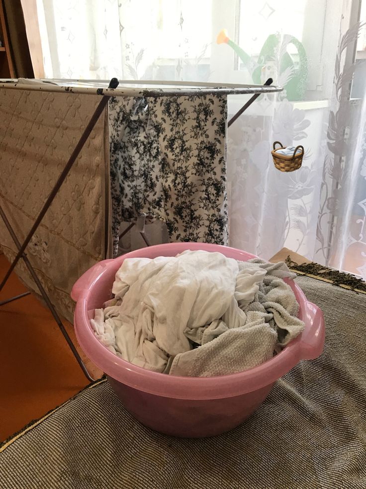 a pink bowl filled with clothes sitting on top of a table next to a window