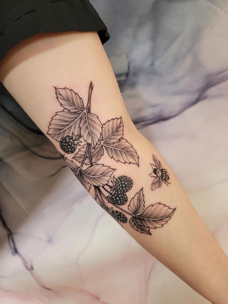 a woman's leg with blackberries and leaves on her left arm, tattoo style