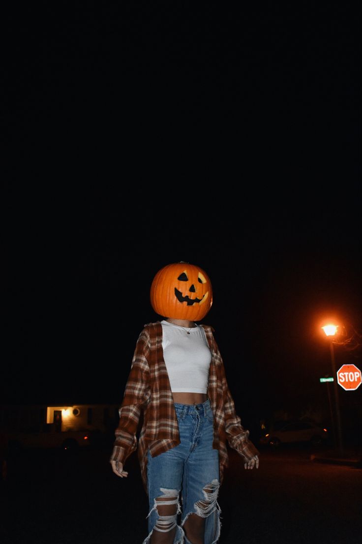 a woman in ripped jeans and a pumpkin hat is walking down the street at night