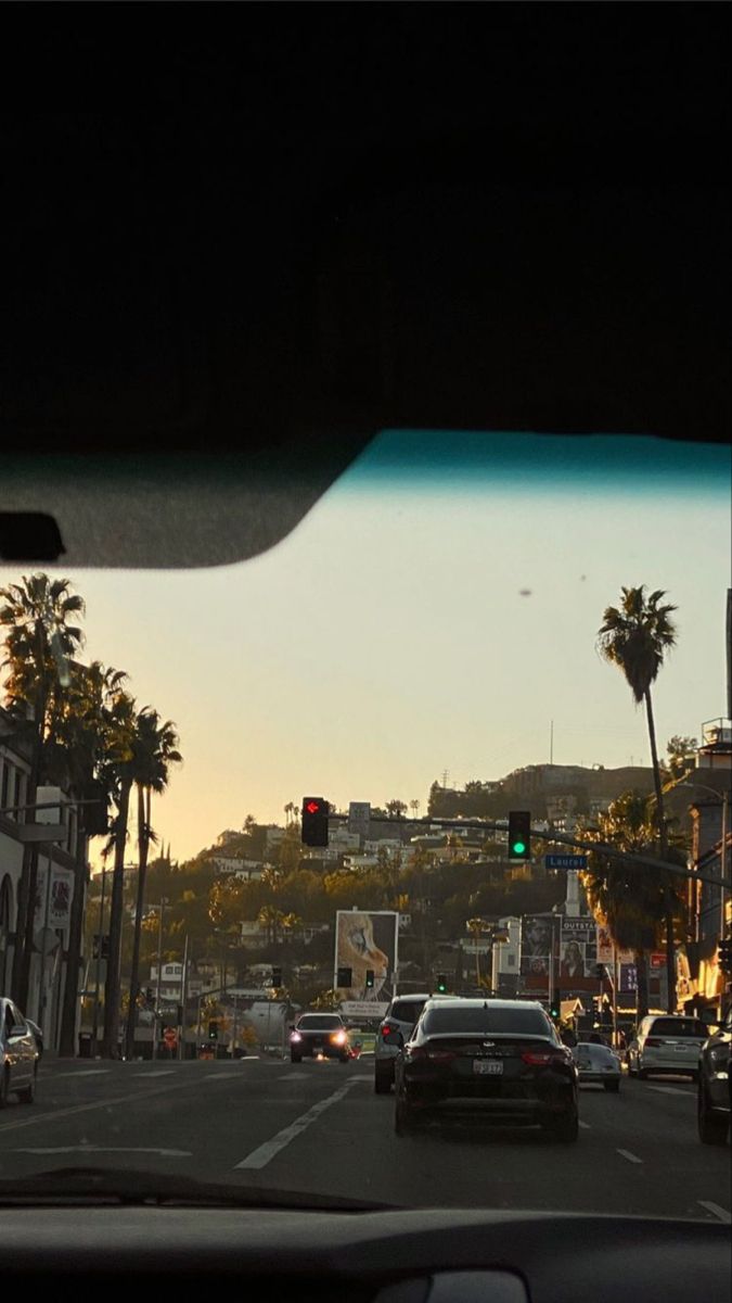 cars are driving down the street in front of tall buildings and palm trees at sunset