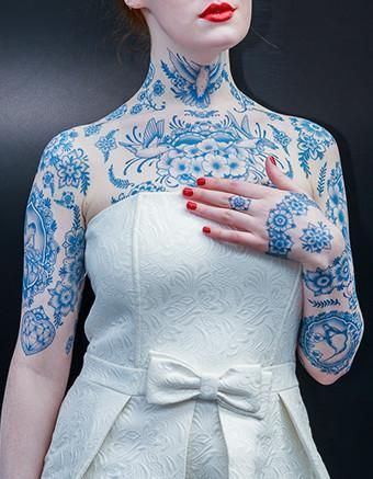 a woman with red hair and tattoos on her body is wearing a white dress that has blue flowers on it