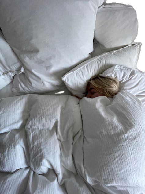 a woman is sleeping in an unmade bed with white sheets and pillows on it