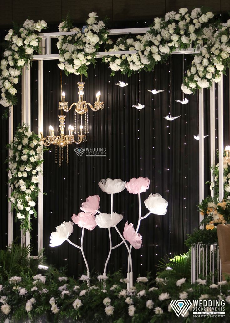 a wedding stage decorated with flowers and chandelier hanging from the ceiling in front of a black backdrop