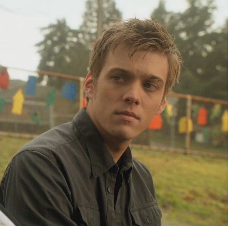 a young man sitting in front of a fence with his hands on his hips and looking at the camera