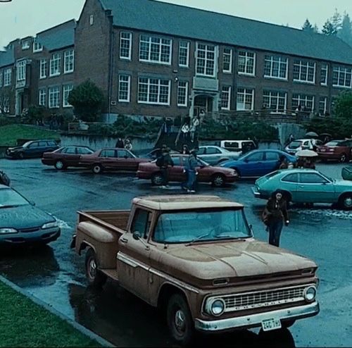 an old truck parked in a parking lot with other cars and people standing around it