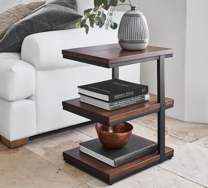 a table with books and a vase on it in front of a white couch next to a potted plant