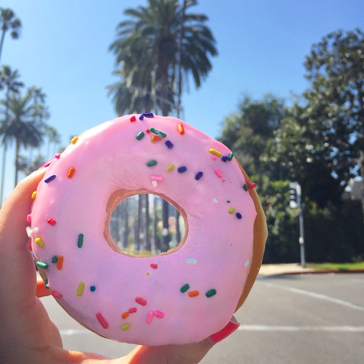 a person holding up a pink frosted donut with sprinkles on it