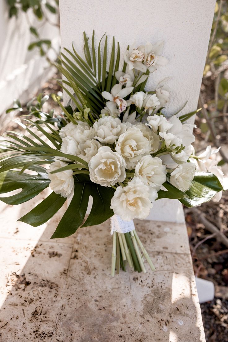 a bouquet of white flowers sitting on top of a stone slab in front of trees