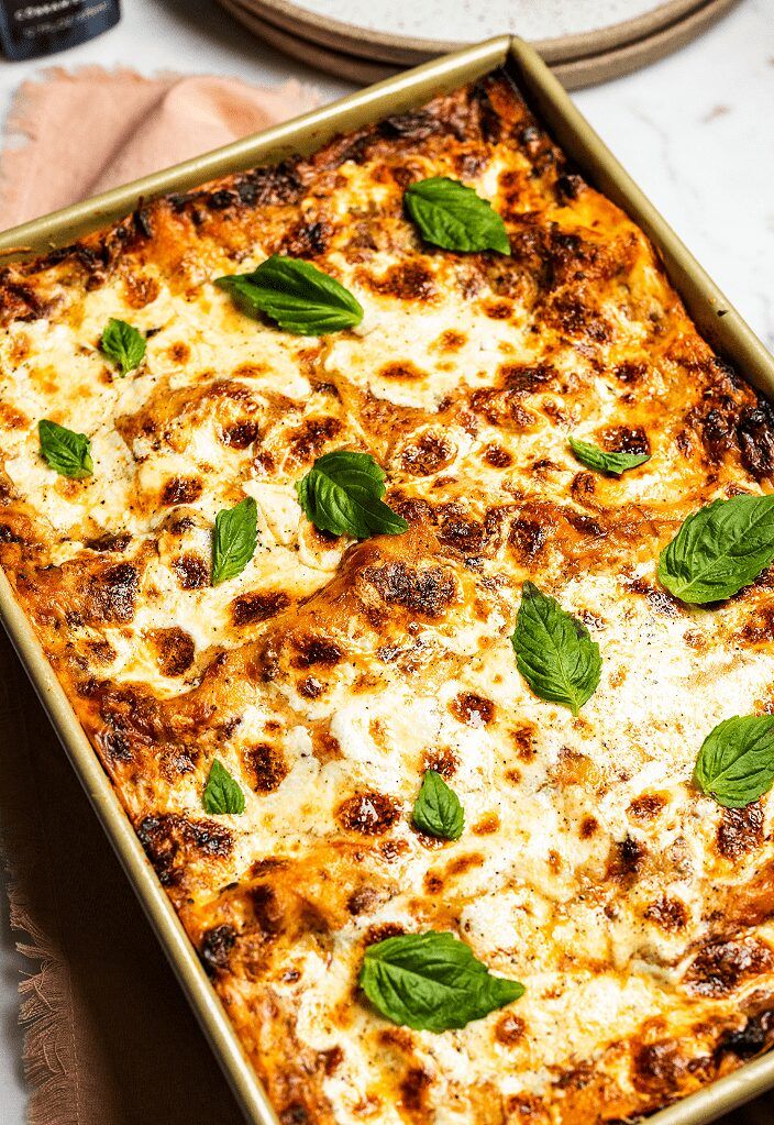 a casserole dish with cheese and spinach leaves on top, sitting on a table