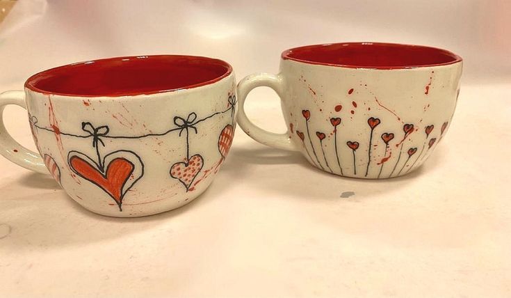 two coffee mugs decorated with hearts and flowers on a white counter top next to each other