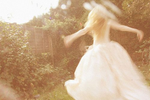 a woman in a white dress is walking through the grass with her arms spread out