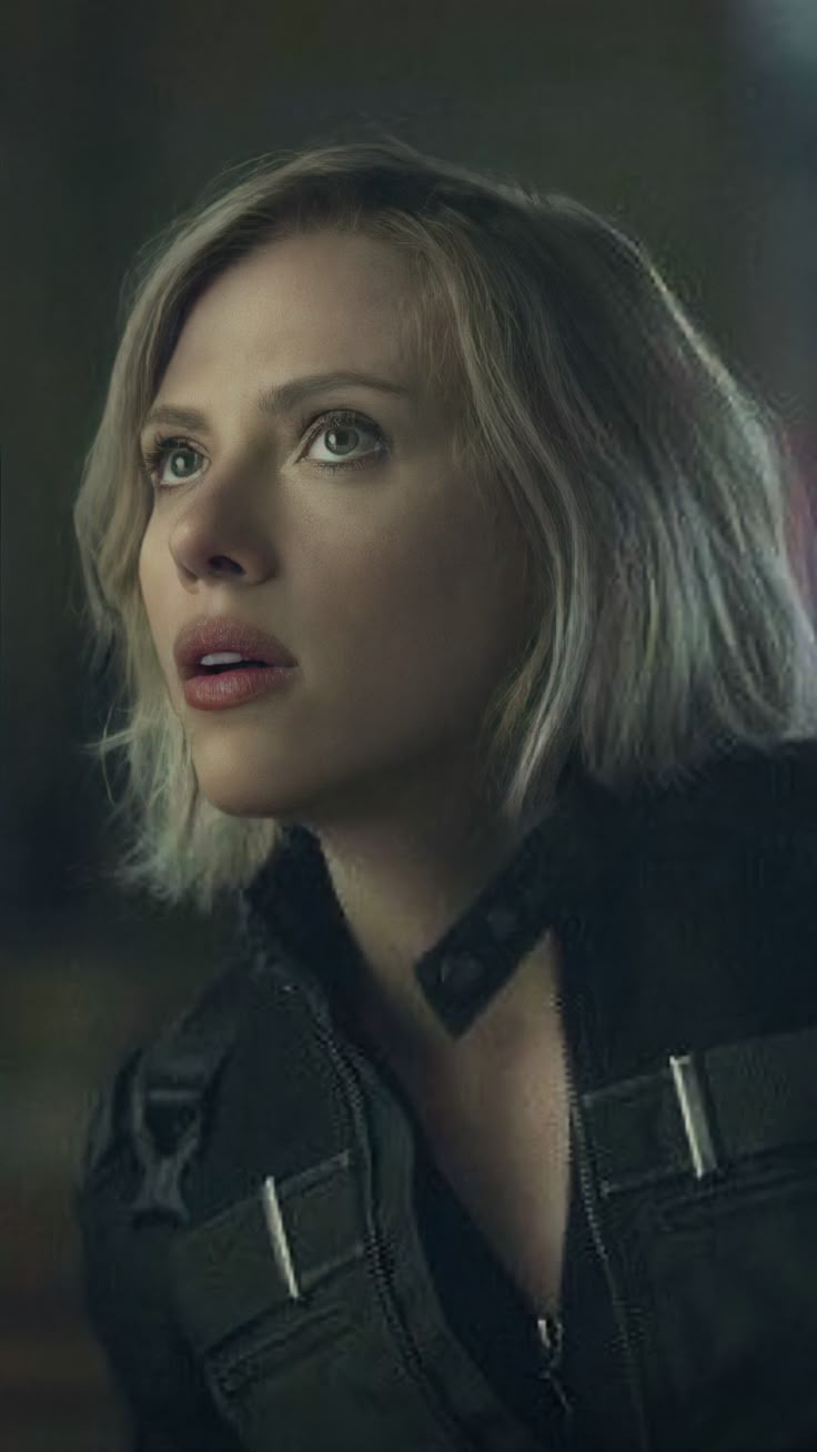 a woman with blonde hair and black jacket looking off to the side in a dark room