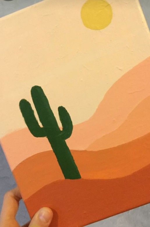 someone is holding up a painting with a cactus in the desert on it's side