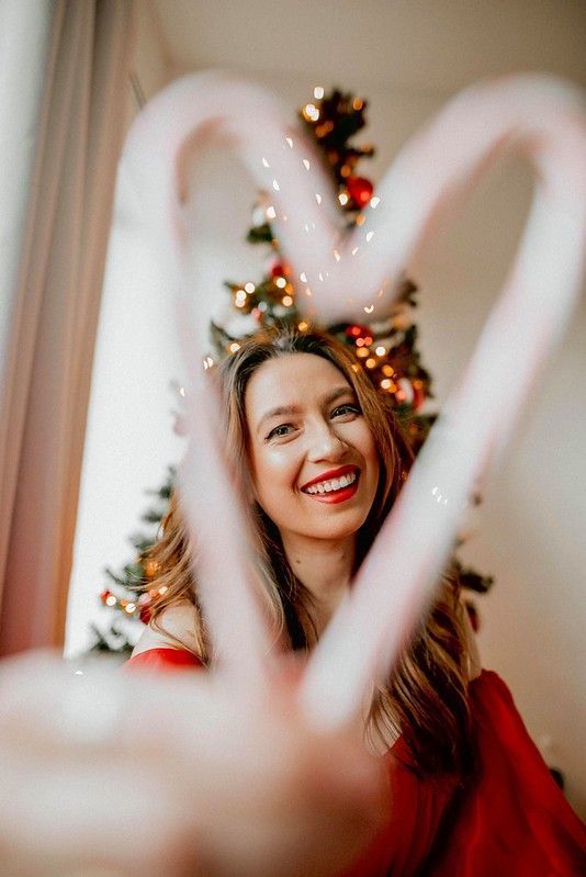 a woman making a heart shape with her hands in front of a christmas tree that has lights on it