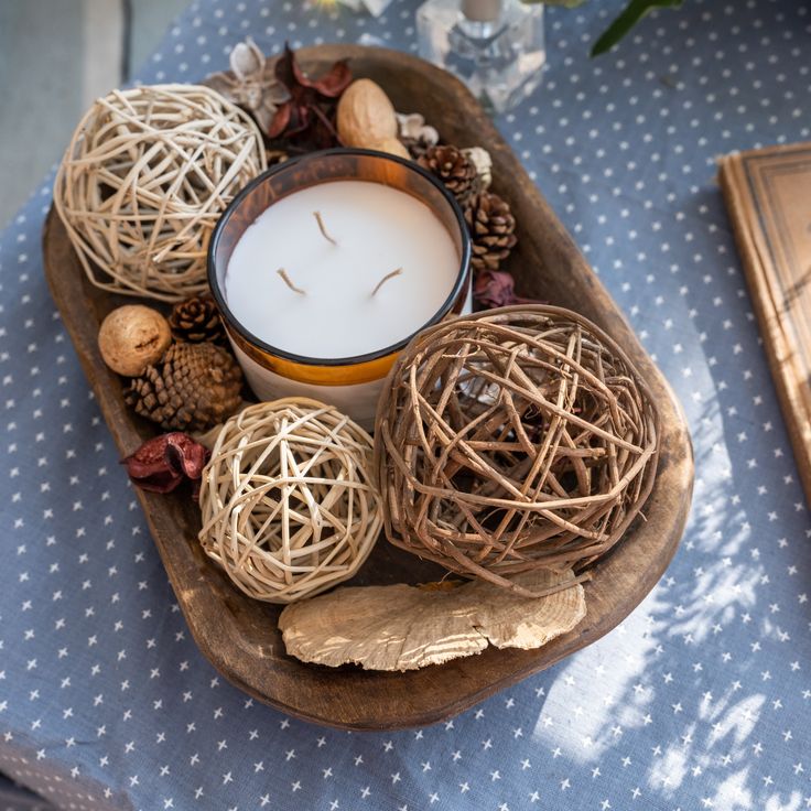 a candle sitting on top of a wooden tray filled with branches and balls next to a book