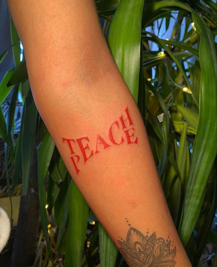 a person's arm with the word peace tattooed on it, in red ink