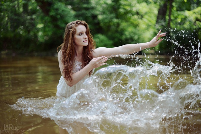 a woman in white dress splashing water on her face while standing in the middle of a river