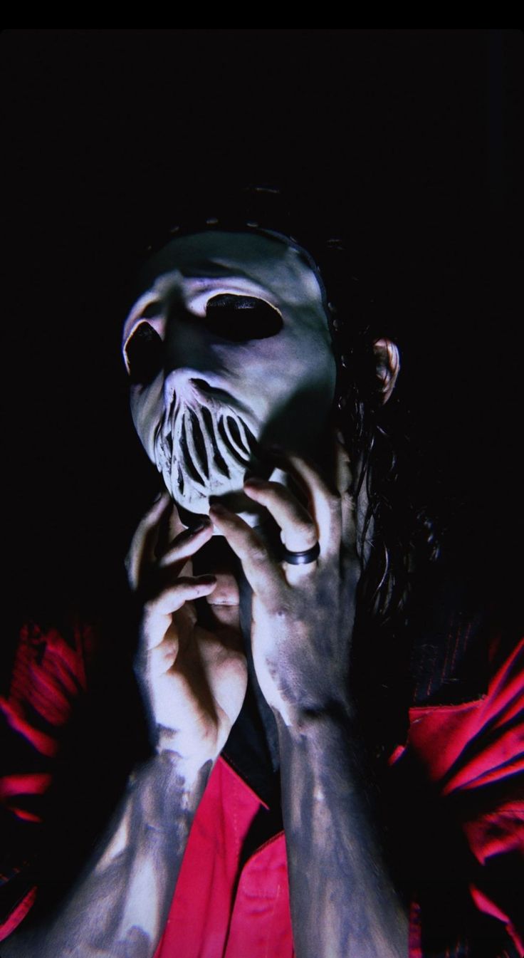 a man with his face painted white and wearing a scary mask, holding his hands to his face