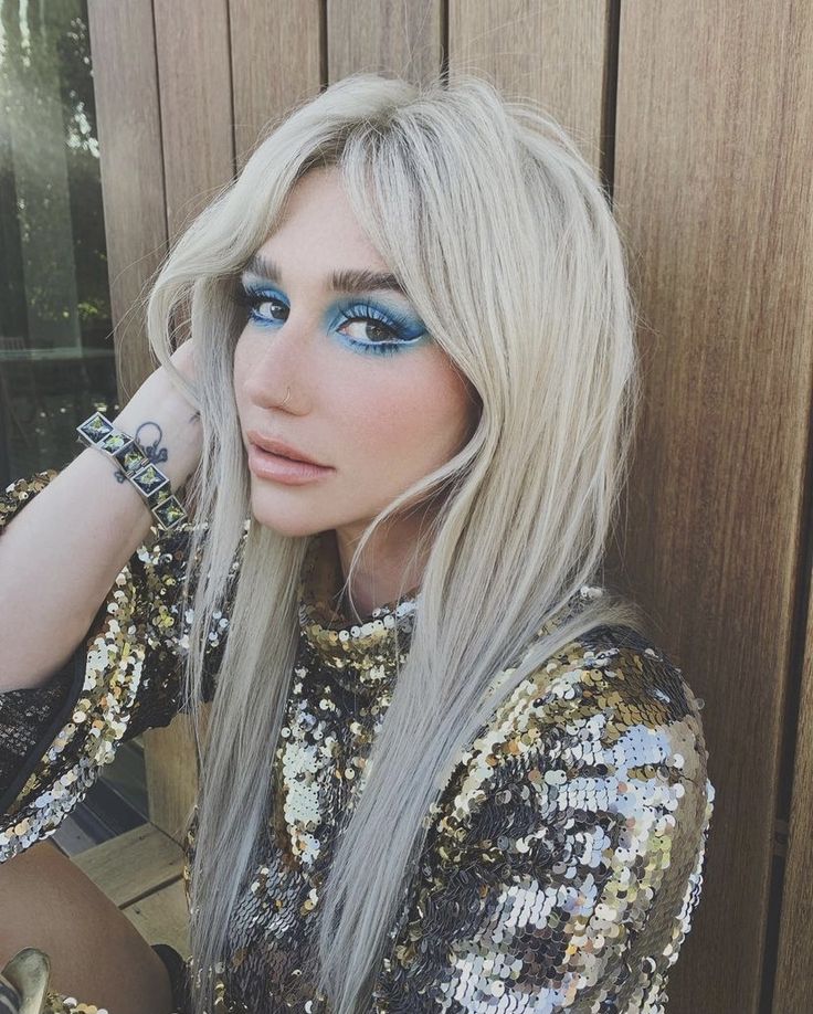 a woman with long blonde hair and blue eyeshade posing in front of a wooden wall